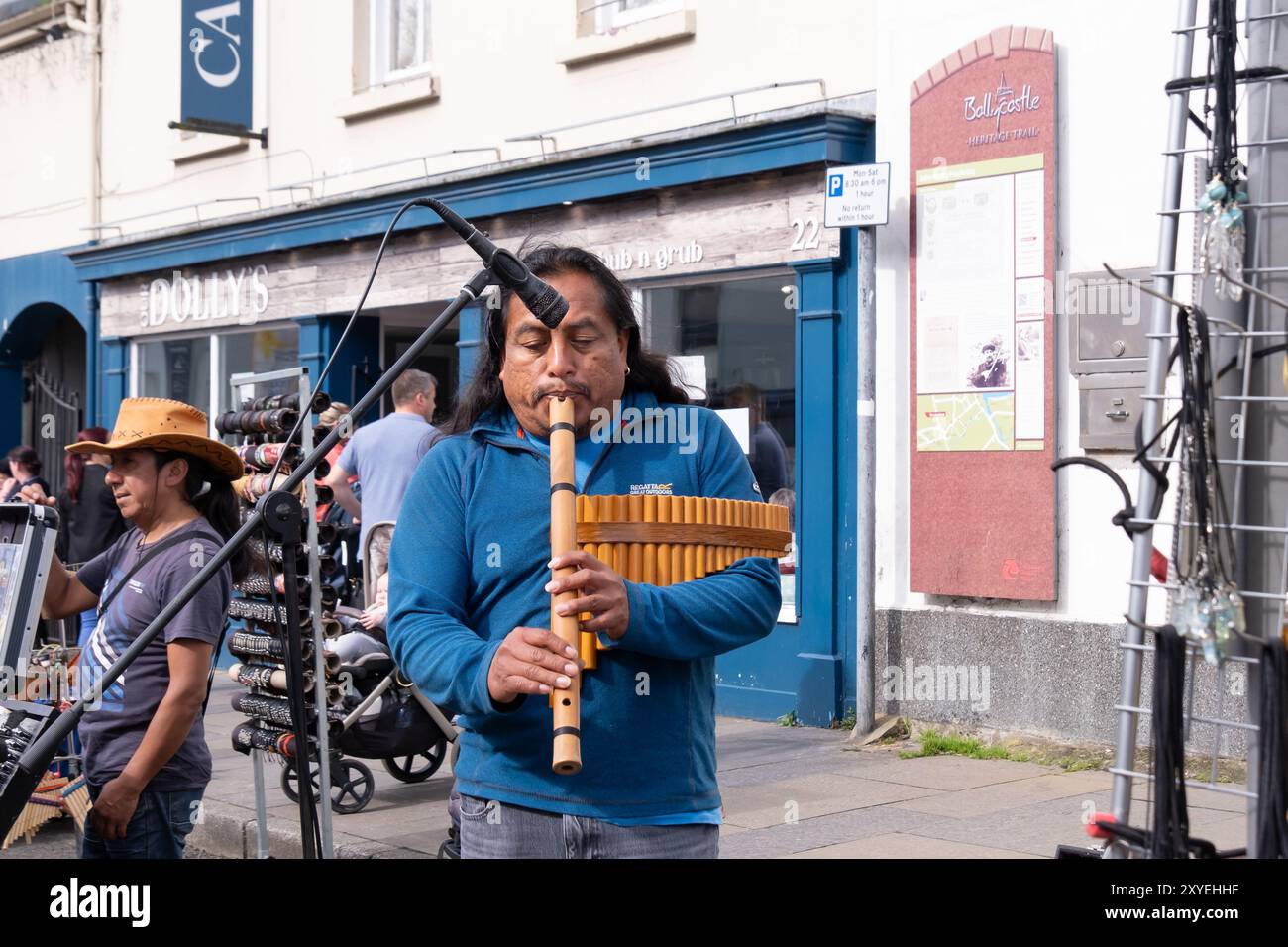 Musique traditionnelle sud-américaine jouée par un homme avec de longs cheveux noirs en haut bleu, tenant des panpipes traditionnelles. Ballycastle, Royaume-Uni - 26 août 2024. Banque D'Images