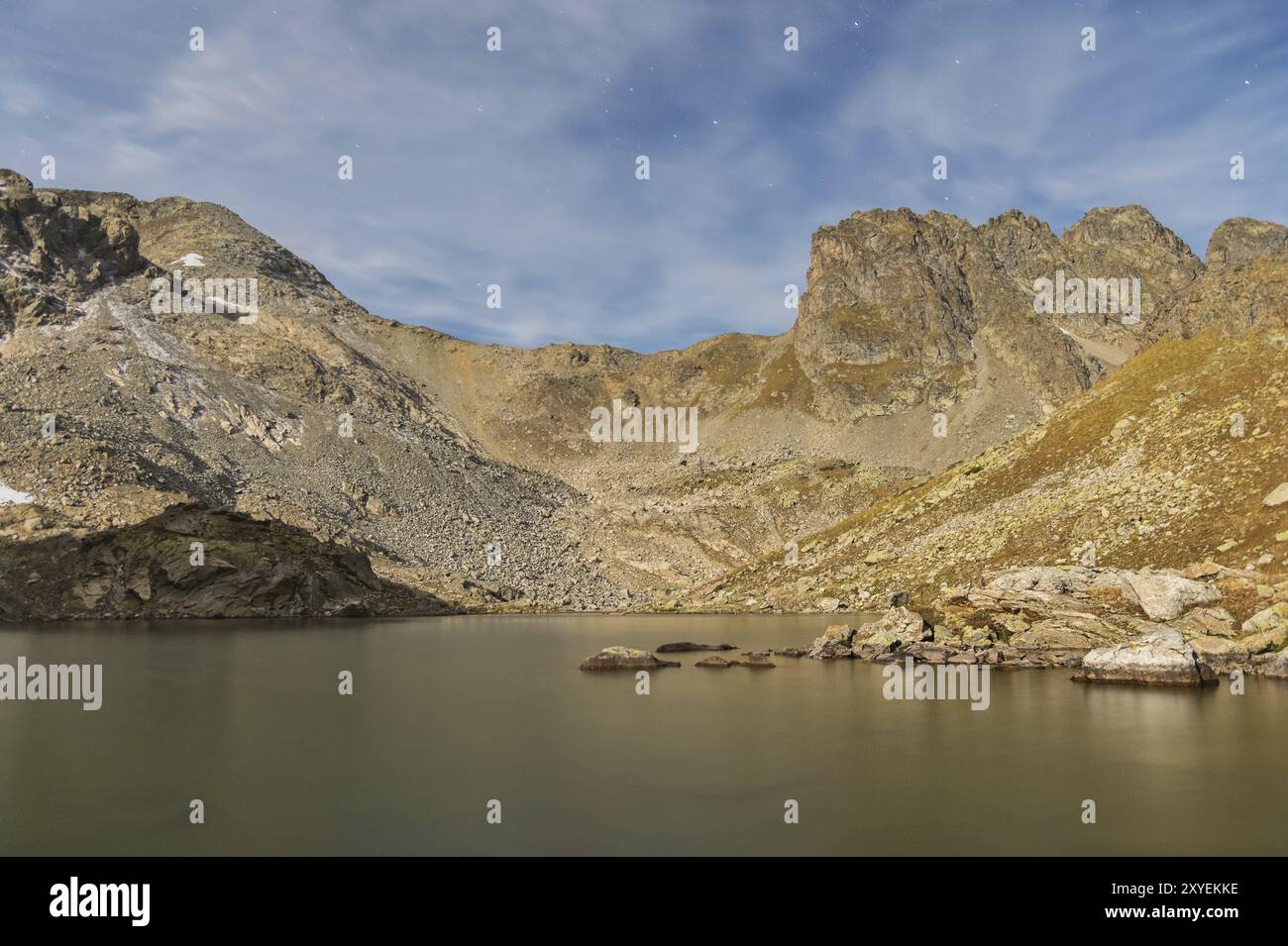 Le paysage de nuit d'un lac de haute montagne avec clair de lune avec des pierres translucides à travers l'eau au fond du lac et des roches acérées dans le Banque D'Images