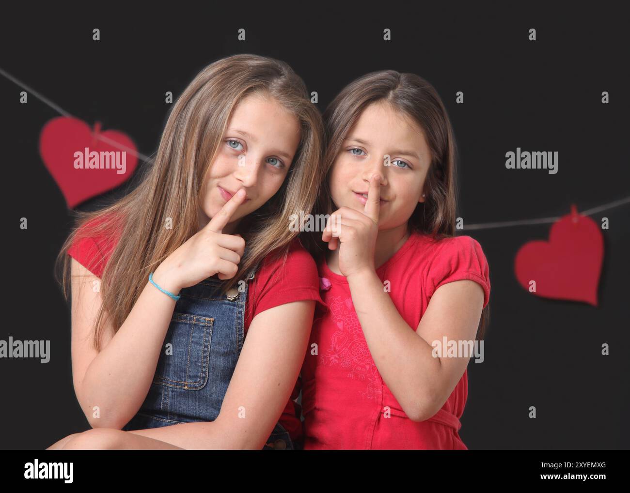 portrait de deux petites filles joyeuses avec geste de silence sur fond noir Banque D'Images