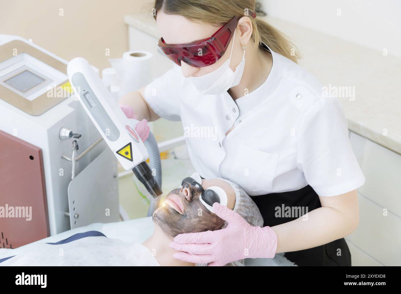 La fille cosméticienne dans des lunettes fait la procédure de peeling au carbone à l'aide d'un laser de cosmétologie. Procédé de pelage de la face en carbone. Impulsion laser Banque D'Images