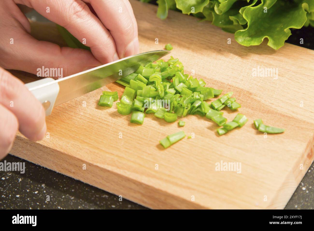 Oignon vert haché et la main avec couteau coupant sur la planche à découper en bois Banque D'Images