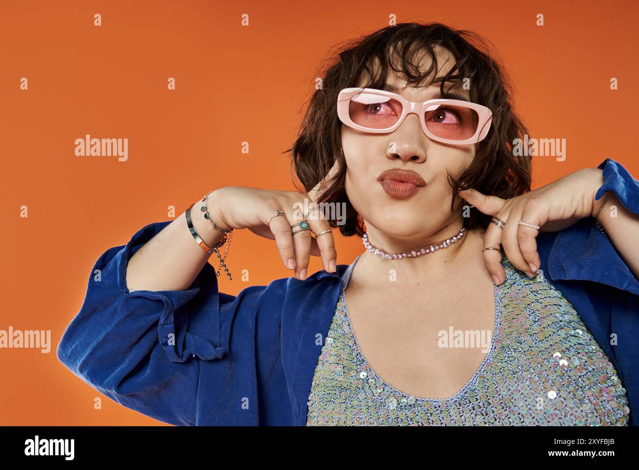 Une femme dans une tenue vibrante prend une pose ludique sur un fond orange vif. Banque D'Images