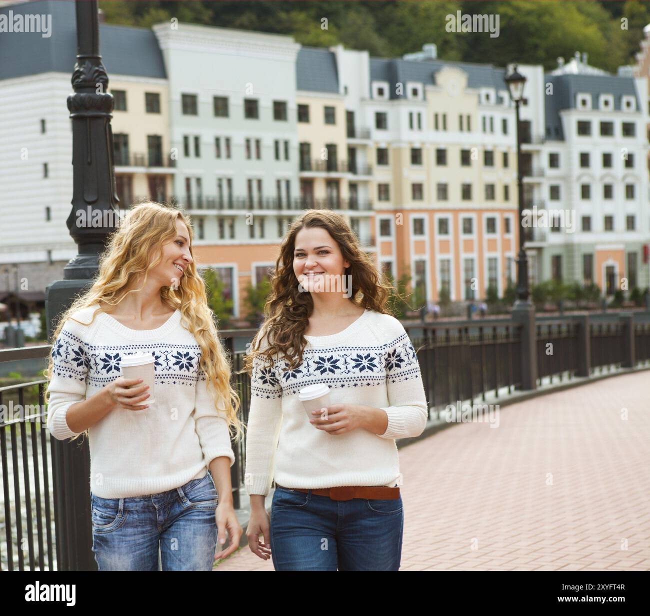 Deux femmes heureux occasionnels ayant une conversation tout en marchant dans la ville avec du café chaud Banque D'Images