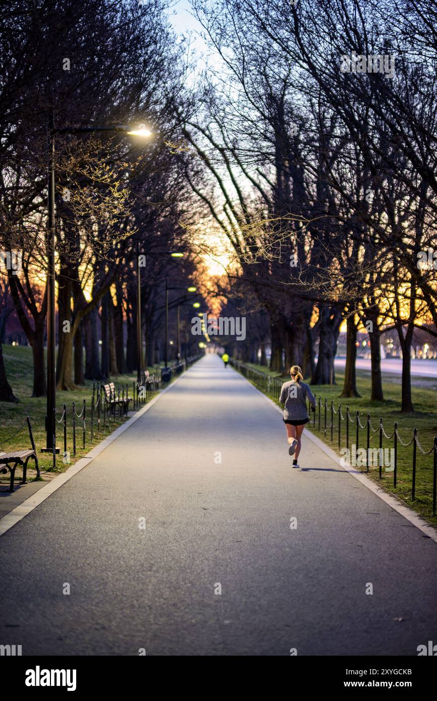 Lincoln Memorial Reflecting Pool Woman Running Washington DC // WASHINGTON DC — Une femme court le long du chemin sur le côté sud du Lincoln Memorial Reflecting Pool sur le National Mall à l'heure précédant l'aube. La scène tôt le matin capture l'atmosphère tranquille de la capitale nationale avant le début de la journée, avec les monuments emblématiques en toile de fond. Banque D'Images