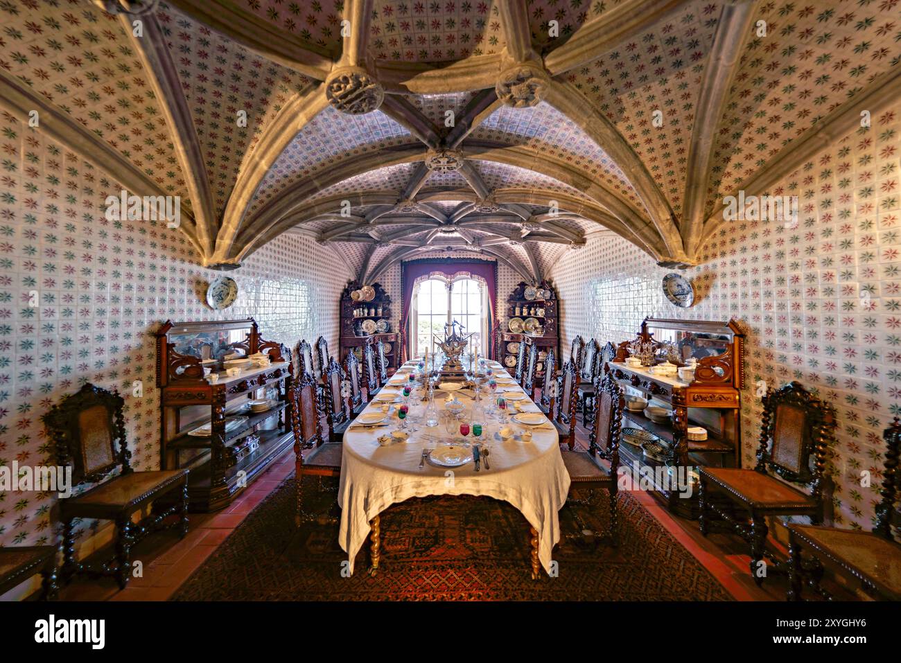 SINTRA, Portugal — la salle à manger du Palais de Pena, anciennement le réfectoire des moines Hiéronymites, convertie par le roi Ferdinand II en salle à manger privée de la famille royale portugaise. La chambre présente des voûtes en côtes manuélines datant du XVIe siècle et est bordée de tuiles du XIXe siècle réalisées par Fábrica Roseira. Le mobilier en chêne, commandé par le roi Ferdinand II en 1866 à Casa Barbosa e Costa, ajoute à l'ambiance historique et royale de l'espace. Banque D'Images