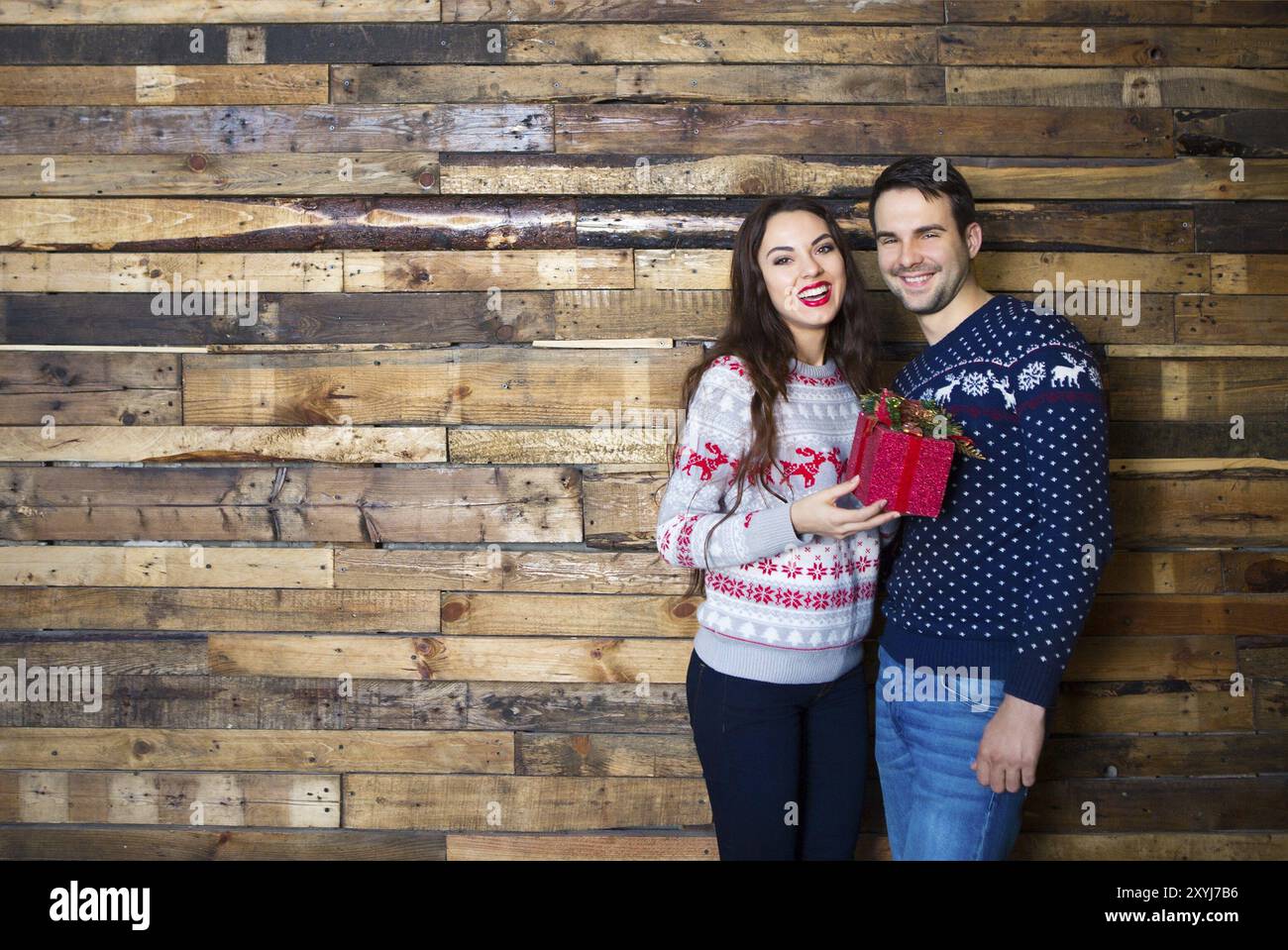 Jeune couple près du mur en bois célébrant Noël avec cadeau. Amour et concept de relation Banque D'Images