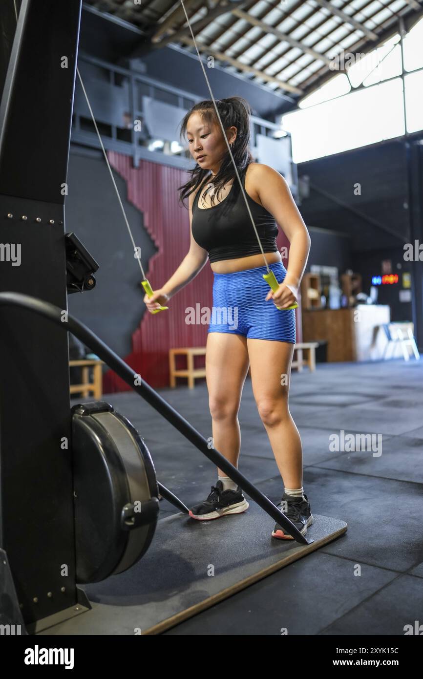 Photo verticale d'une forte femme chinoise exerçant avec des poids dans une machine à tirer lat Banque D'Images