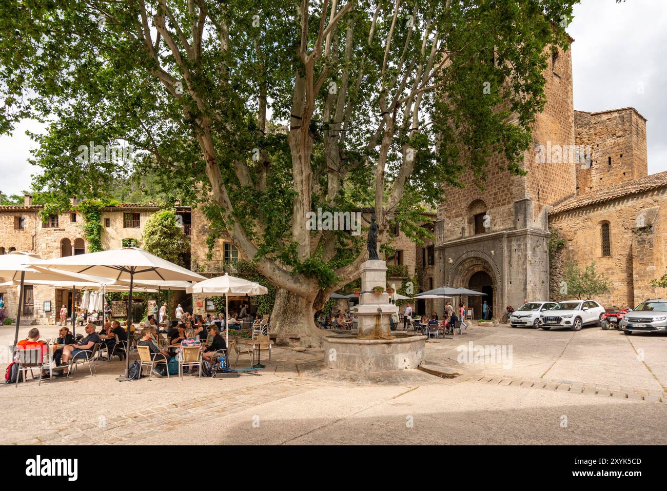 Les gens au café en plein air sur la place du village de la liberté, St Guilhem le désert, Hérault, Occitanie, France, Europe Banque D'Images