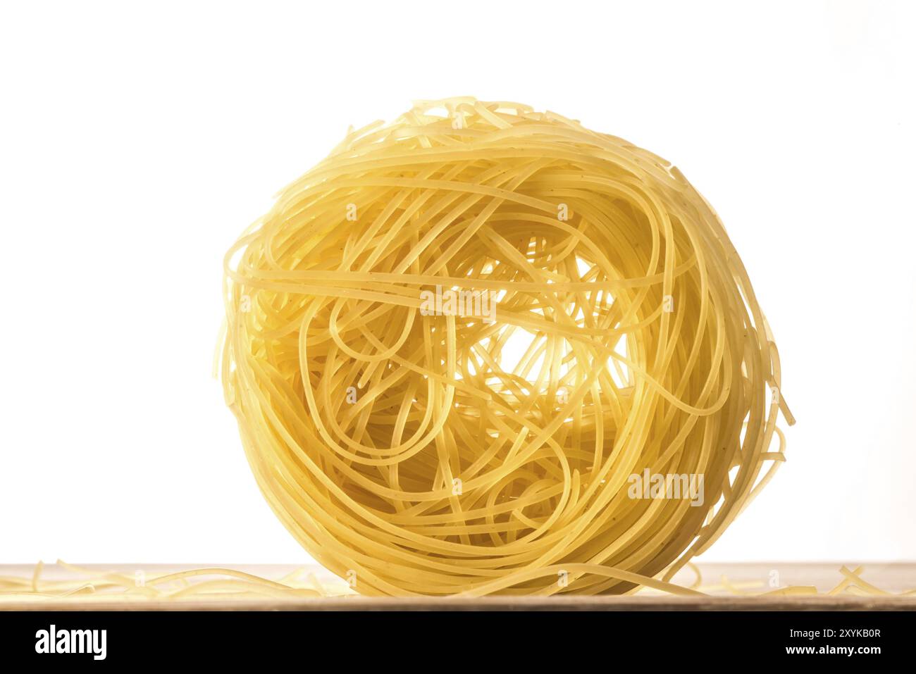 Une seule boule de spaghettis secs et non cuits de cheveux d'Angel sur une surface en bois devant un fond blanc brillant Banque D'Images