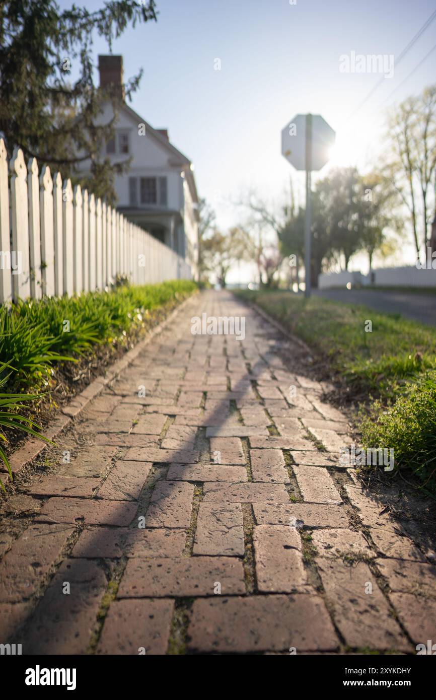 Trottoir de briques le long de la clôture blanche de piquetage dans le soleil du soir Banque D'Images