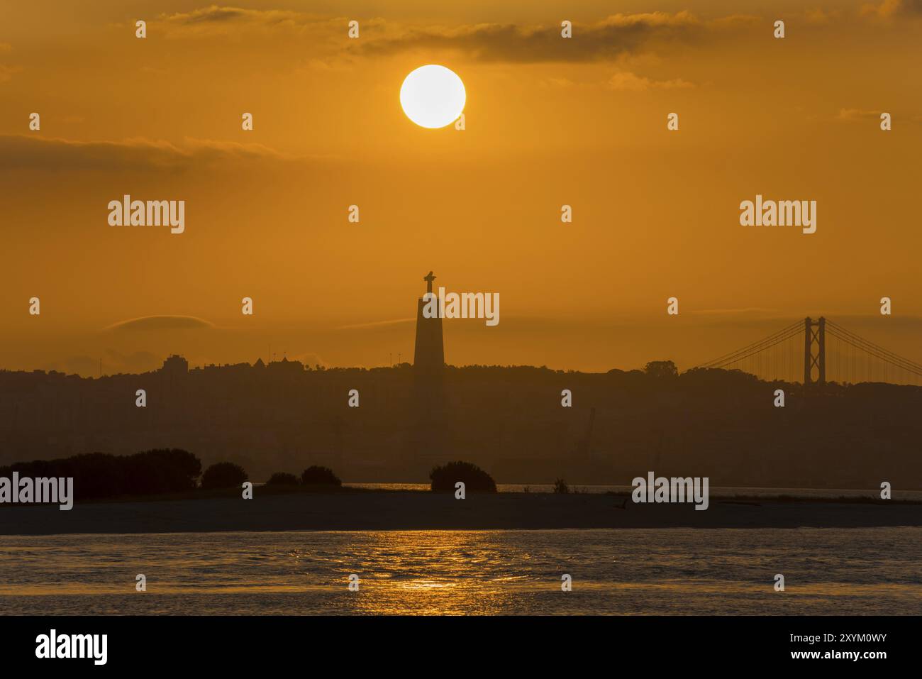 Scène atmosphérique avec un coucher de soleil sur une statue et un pont baignant l'eau dans la lumière dorée, Statue Cristo Rei, Ponte 25 de Abril, Pont du 25 avril Banque D'Images