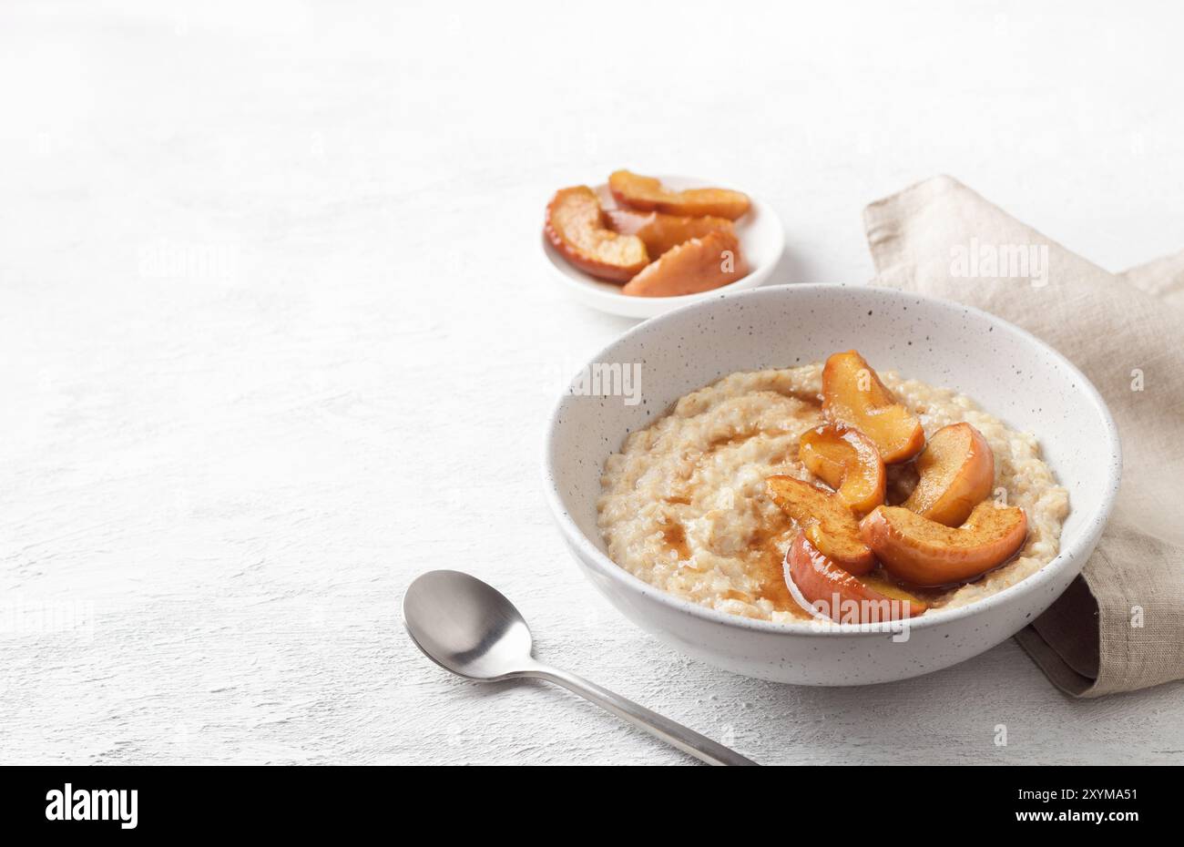 Bouillie d'avoine sucrée avec tranches de pomme cuites au four, cannelle et sauce caramel dans un bol gris sur fond clair Banque D'Images