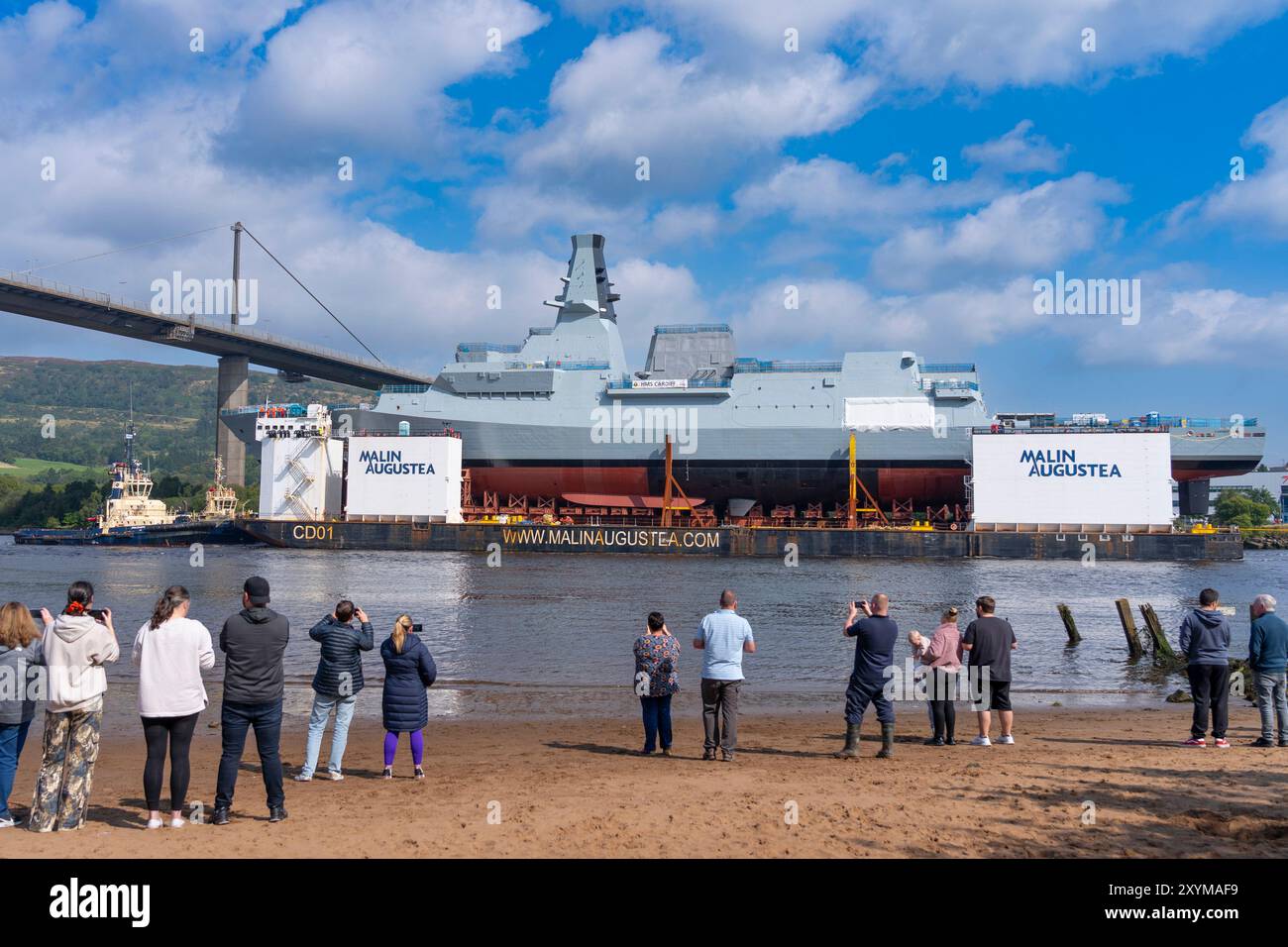 Erskine, Écosse, Royaume-Uni. 30 août 2024. La frégate HMS Cardiff type 26 a été lancée sur une barge au chantier naval BAE Systems à Govan, Glasgow. Le navire de guerre est transporté par barge à Glenmallan sur le Loch long où il sera déchargé de la barge. Par la suite, il sera remorqué au chantier naval BAE à Yoker pour être aménagé à côté de son navire jumeau HMS Glasgow. Pic ; HMS Cardiff au pont Erskine surveillé par des membres du public. Iain Masterton/Alamy Live News Banque D'Images