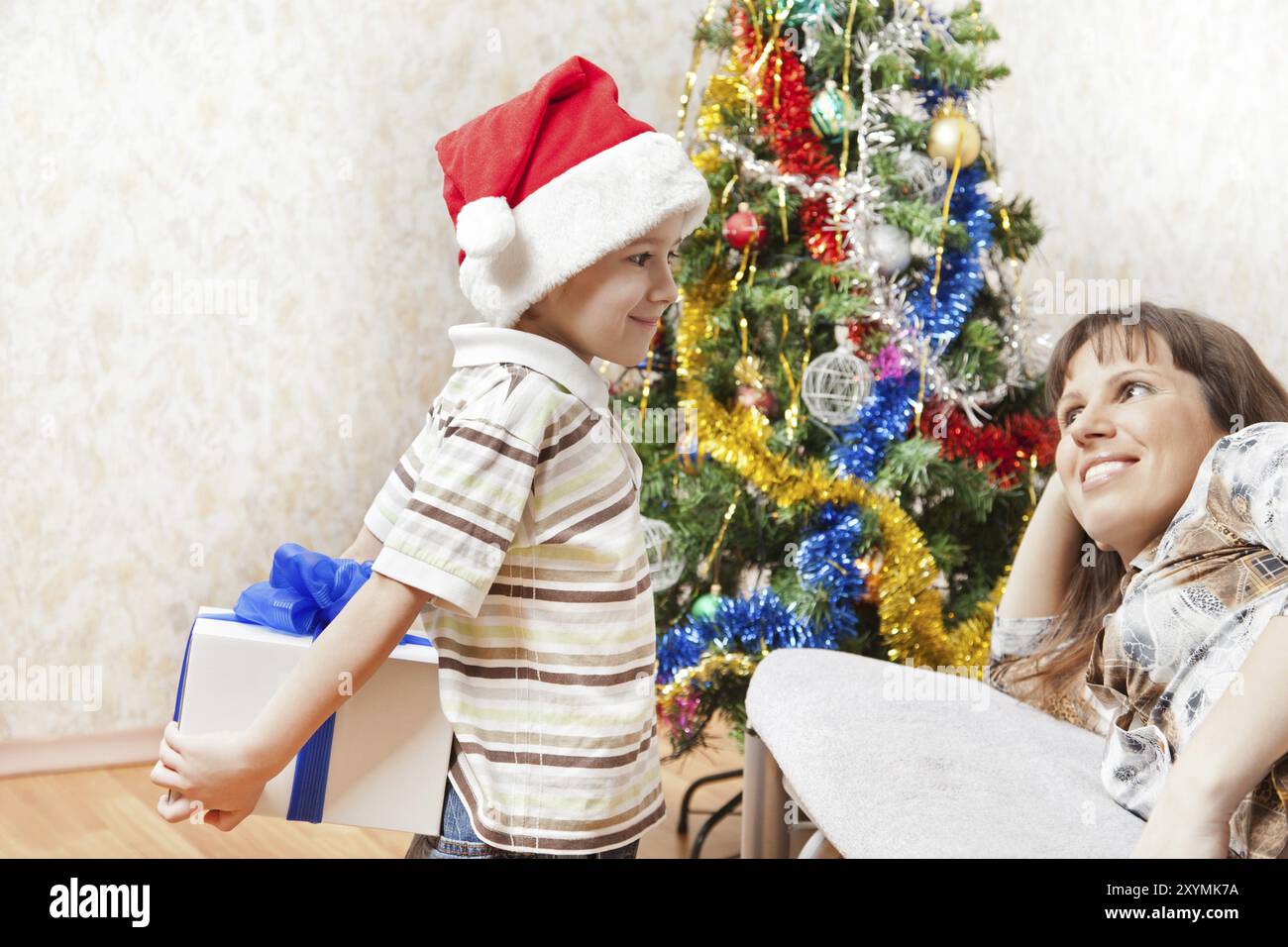 Petit fils portant chapeau de Père Noël donnant cadeau du nouvel an ou boîte cadeau de noël à mère souriante Banque D'Images