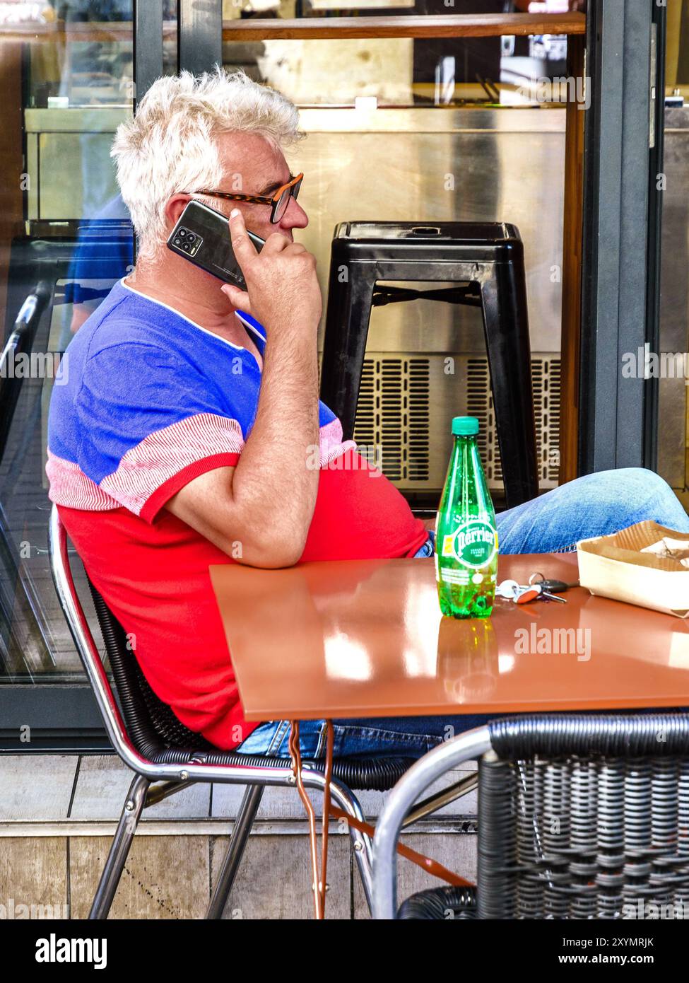 Homme assis à la table de café en plein air écoutant smartphone - Tours, Indre-et-Loire (37), France. Banque D'Images