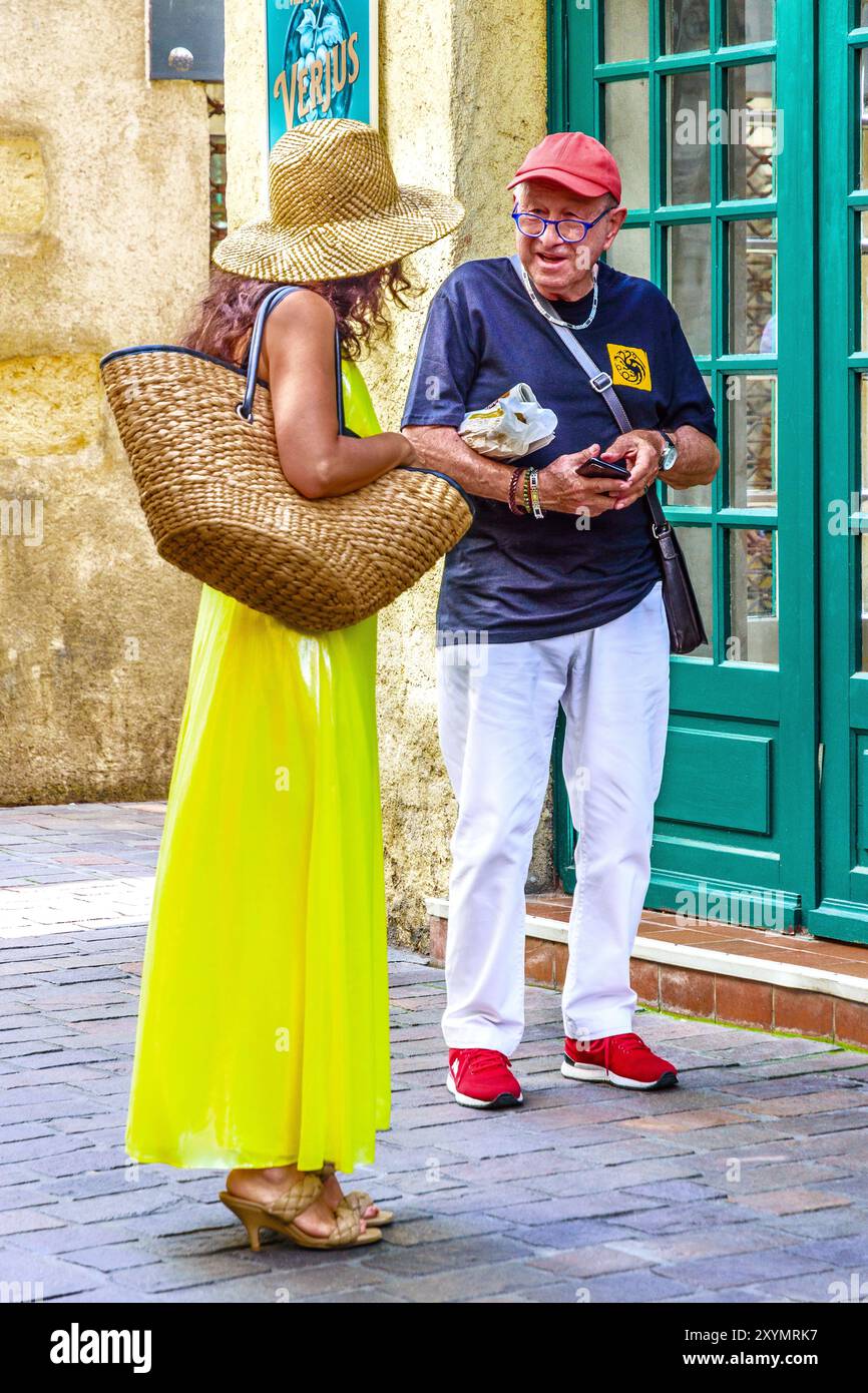 Homme âgé parlant avec une femme en robe PVC jaune vif (plastique) - Tours, Indre-et-Loire (37), France. Banque D'Images