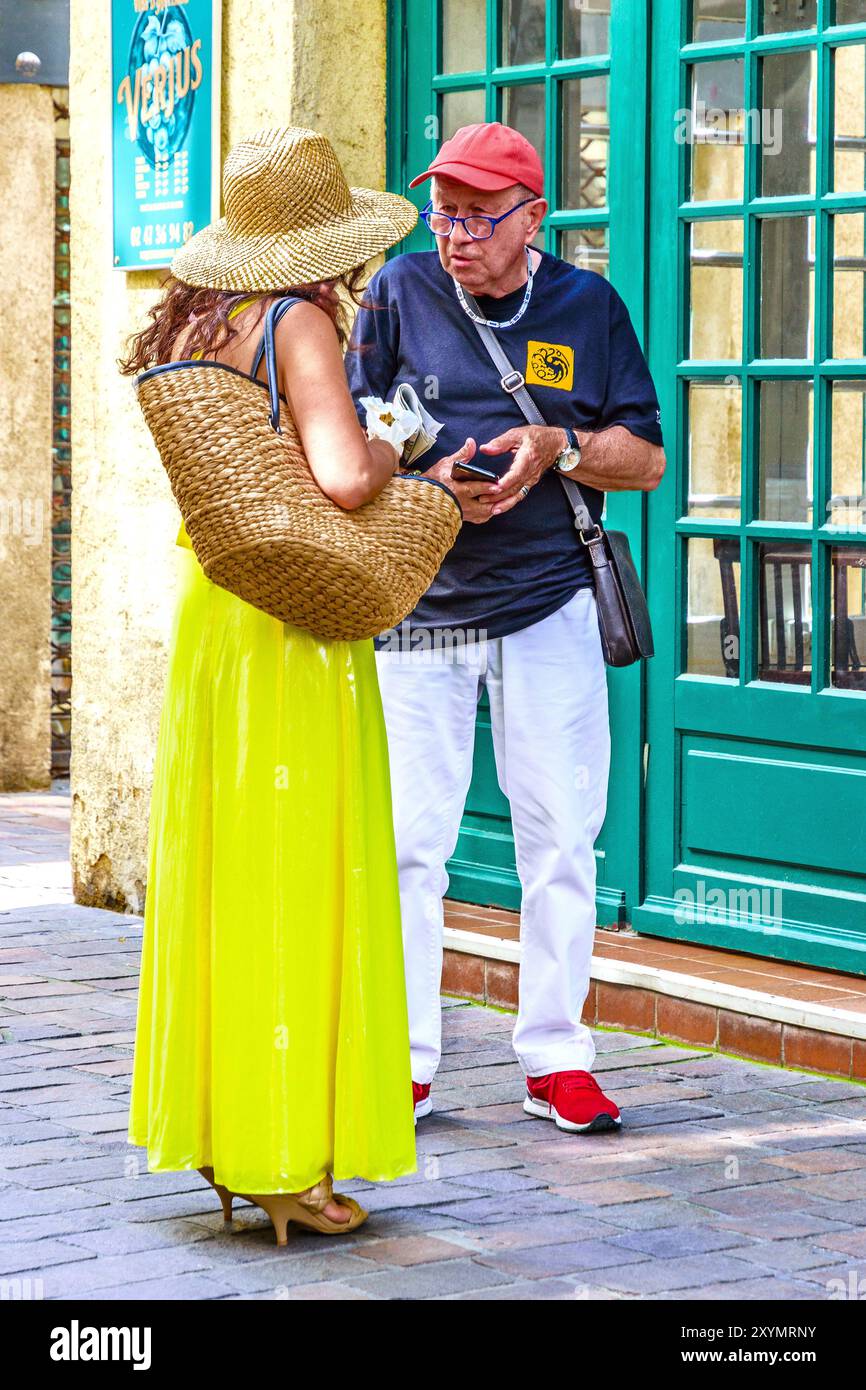 Homme âgé parlant avec une femme en robe PVC jaune vif (plastique) - Tours, Indre-et-Loire (37), France. Banque D'Images