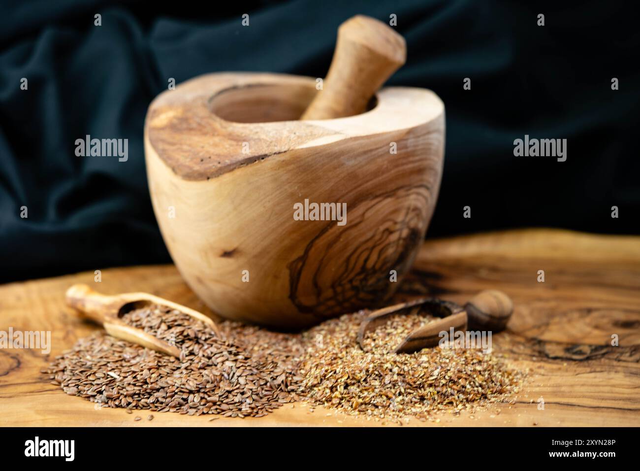 Lin commun (Linum usitatissimum), graines de lin, entières et grossièrement moulues, sur une pelle en bois, avec un mortier et un pilon Banque D'Images