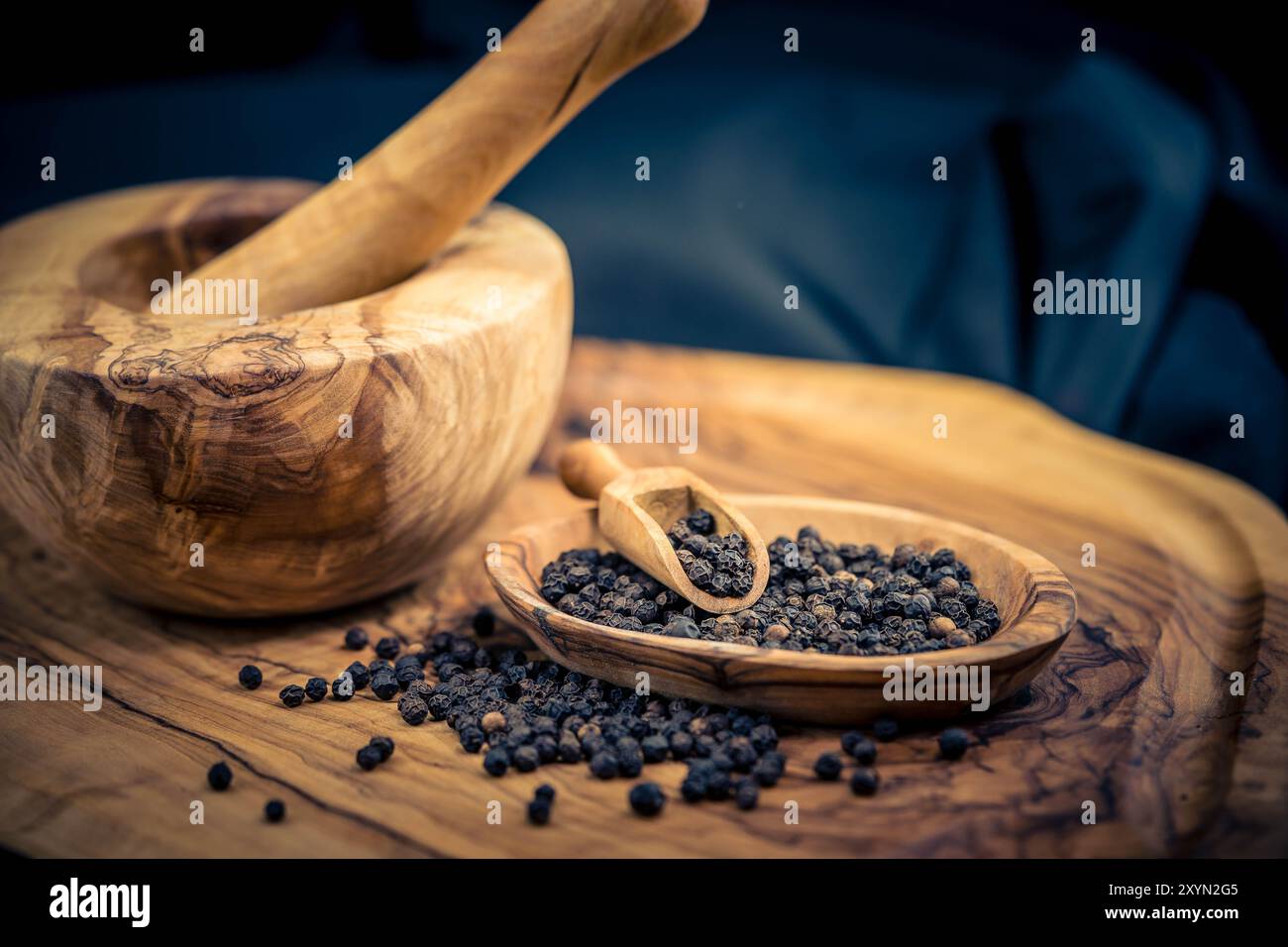 Poivre noir (Piper nigrum), poivre noir sur une assiette avec une pelle en bois et du mortier Banque D'Images