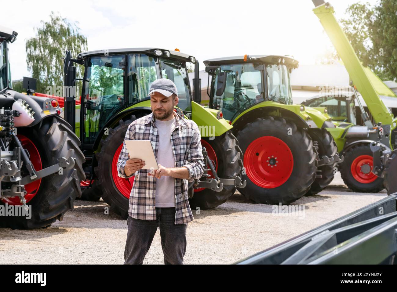 Agro-industrie. Revendeur de matériel agricole et de construction. L'homme se tient contre les nouveaux tracteurs et l'utilisation de la tablette numérique. Banque D'Images