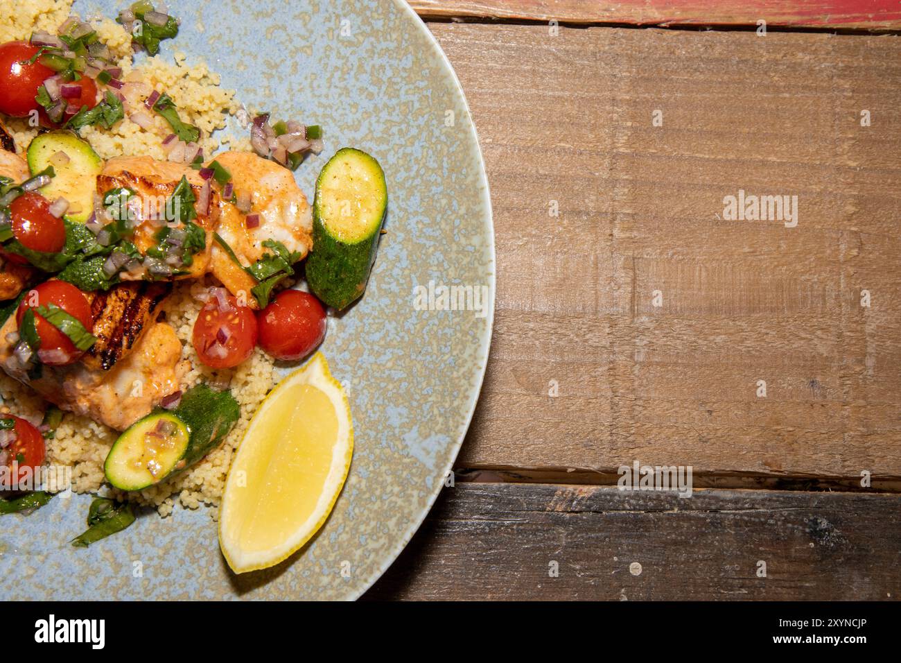 Une délicieuse assiette de saumon de printemps et de brochettes de crevettes avec salade de couscous et salsa aux agrumes sur une table de cuisine en bois Banque D'Images