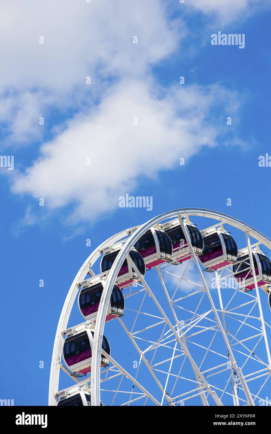 Les nacelles d'une grande roue sont placées en face d'un fond de ciel bleu et de nuages blancs, vus d'en bas Banque D'Images