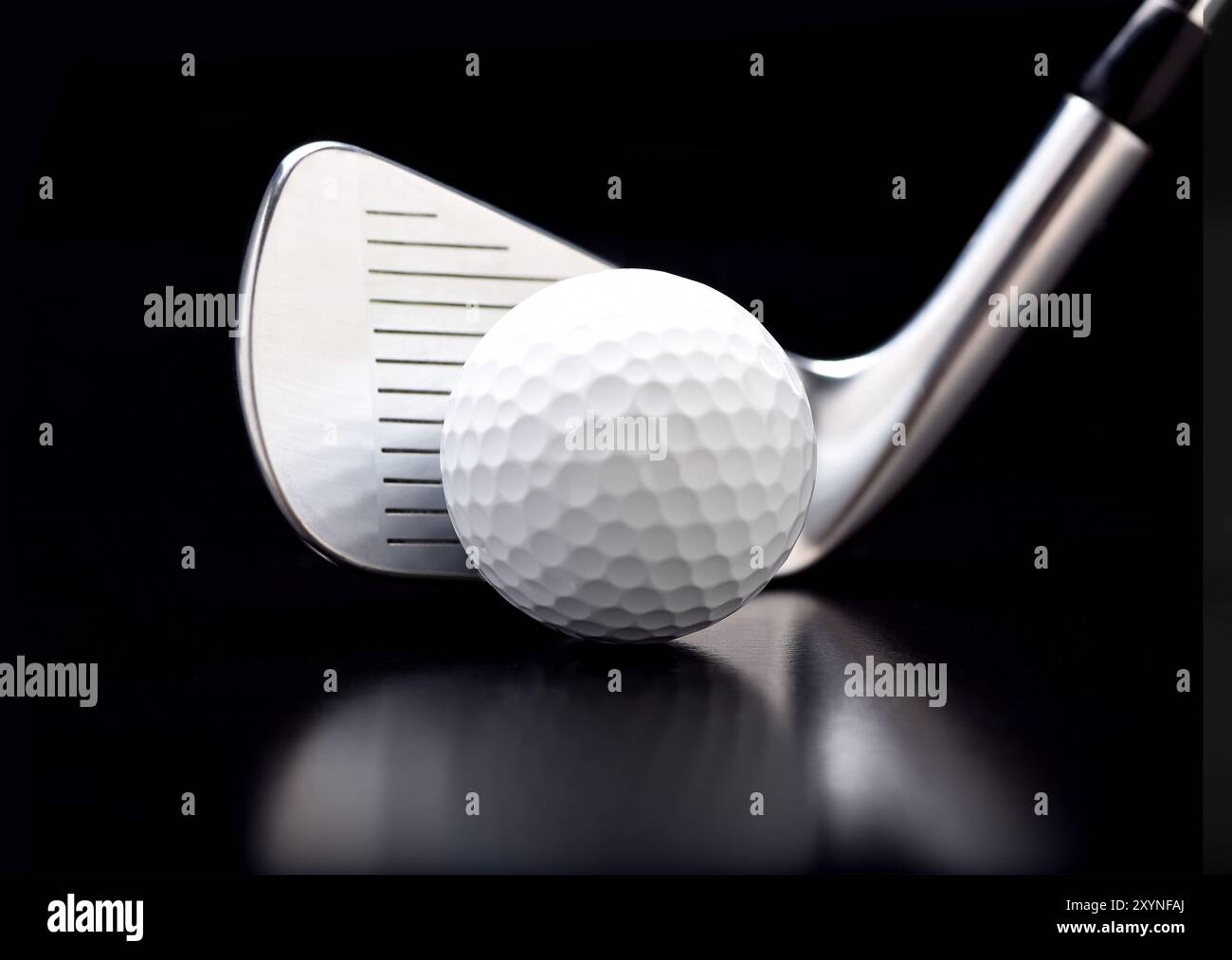 Gros plan d'un fer neuf avec une balle de golf sur noir avec réflexion. Banque D'Images