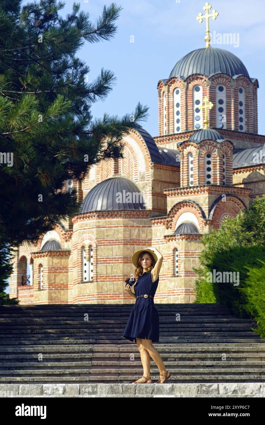 Une femme se tient debout avec un appareil photo reflex numérique devant une église. Femme touriste au monastère Hercegovacka Gracanica (Trebinje, Bosnie-Herzégovine). Banque D'Images