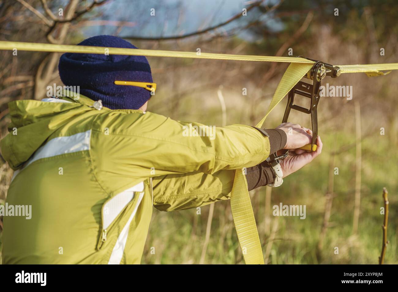 Gros plan mains d'Un homme ajuste le slackline de l'équipement avant d'effectuer des tours de slackline folles et de marcher sur un slacklin dans un parc dans le nat Banque D'Images