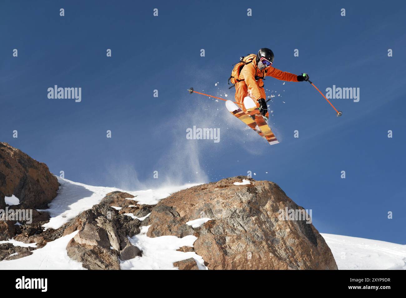 Un skieur professionnel fait un saut-drop d'une haute falaise contre le ciel bleu laissant une piste de poudreuse dans les montagnes. Photo des pistes o Banque D'Images