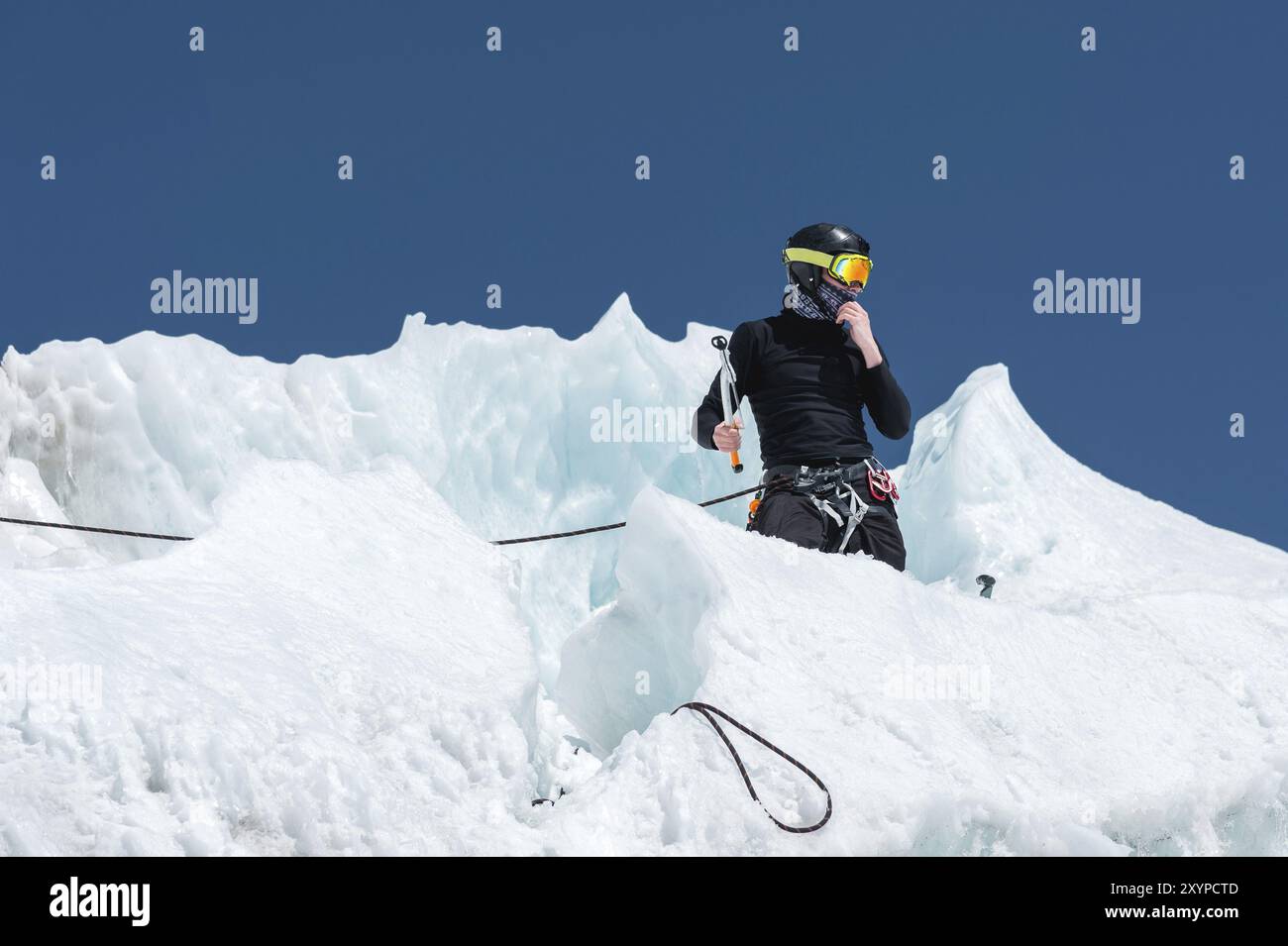 Un alpiniste professionnel portant un casque et un masque de ski sur l'assurance entaille la hache de glace dans le glacier. Le travail d'un grimpeur professionnel en Winte Banque D'Images