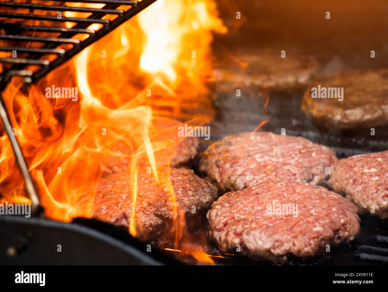 Cuisson des hamburgers sur un gril chaud avec des flammes - galettes hamburger grillées à la flamme. Les hamburgers sont un barbecue traditionnel d'été. Banque D'Images