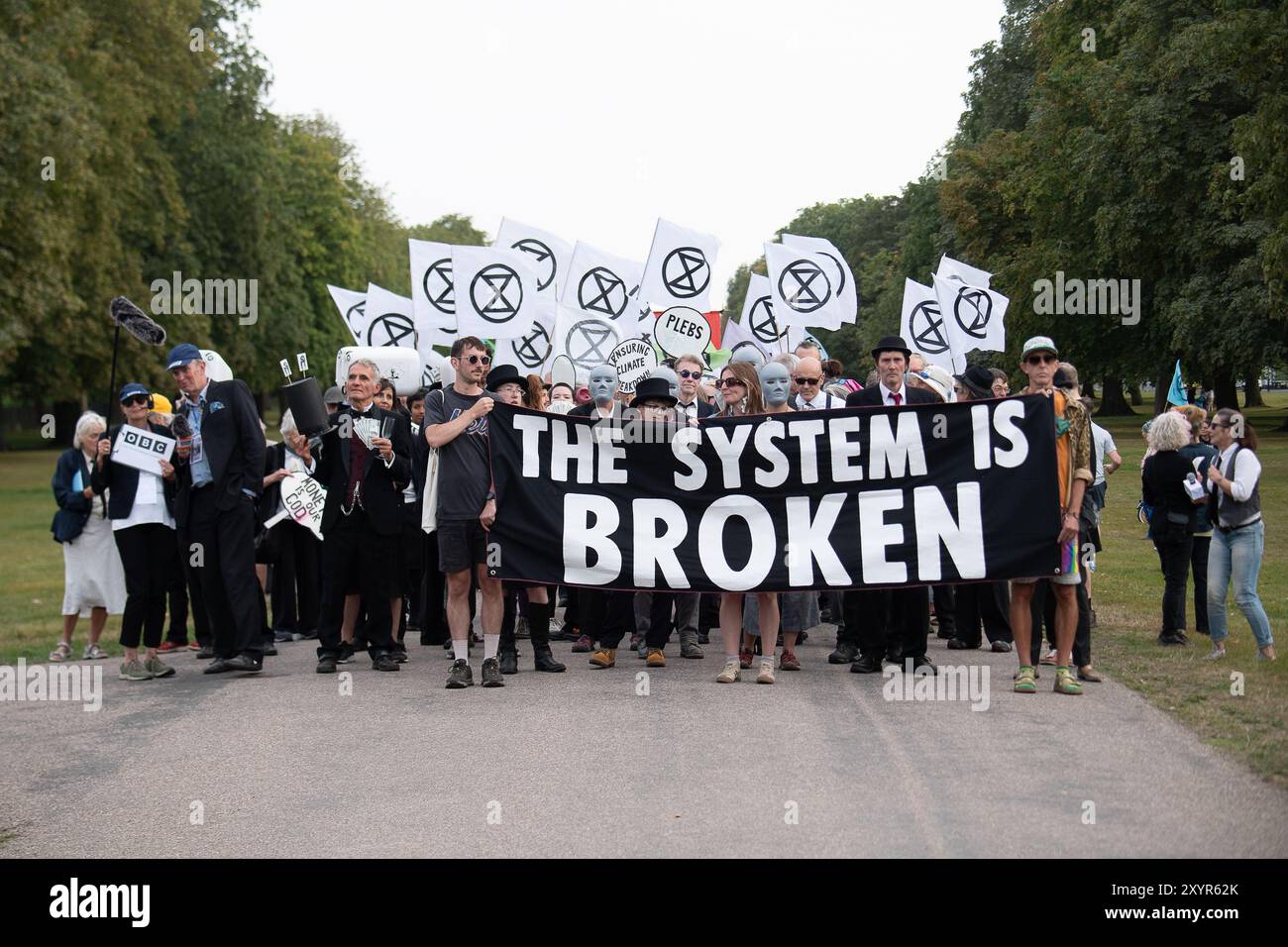 Windsor, Royaume-Uni. 30 août 2024. Extinction Rebellion a organisé une manifestation sur la longue marche avec pour toile de fond le château de Windsor à Windsor, Berkshire ce soir. Les manifestants climatiques de XR portaient des costumes d'affaires et s'habillaient en barons du pétrole, en magnats des médias et en financiers sans visage. Les Oil Slicks, habillés de costumes noirs avec de la peinture de visage noir et blanc, ont réalisé une action théâtrale chorégraphiée dans le but de mettre en évidence le récit XR pour la journée, que le système est brisé. Les rebelles XR campent à Home Park en face du château de Windsor aujourd'hui et pendant le week-end dans le cadre de leur surclassement de trois jours Banque D'Images