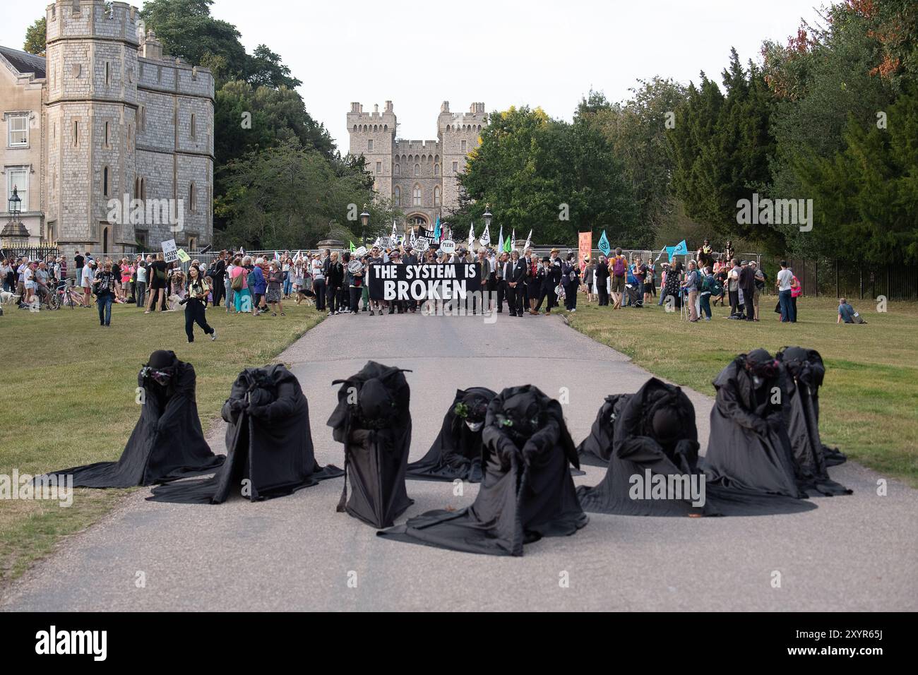 Windsor, Royaume-Uni. 30 août 2024. Extinction Rebellion a organisé une manifestation sur la longue marche avec pour toile de fond le château de Windsor à Windsor, Berkshire ce soir. Les manifestants climatiques de XR portaient des costumes d'affaires et s'habillaient en barons du pétrole, en magnats des médias et en financiers sans visage. Les Oil Slicks, habillés de costumes noirs avec de la peinture de visage noir et blanc, ont réalisé une action théâtrale chorégraphiée dans le but de mettre en évidence le récit XR pour la journée, que le système est brisé. Les rebelles XR campent à Home Park en face du château de Windsor aujourd'hui et pendant le week-end dans le cadre de leur surclassement de trois jours Banque D'Images