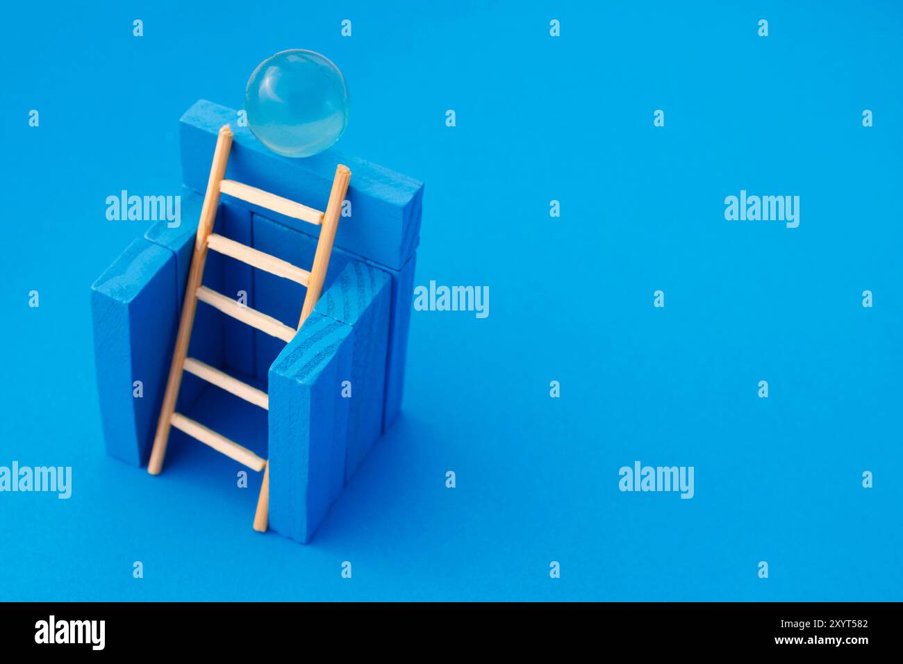 Échelle atteignant une sphère bleue qui est sur un mur Banque D'Images