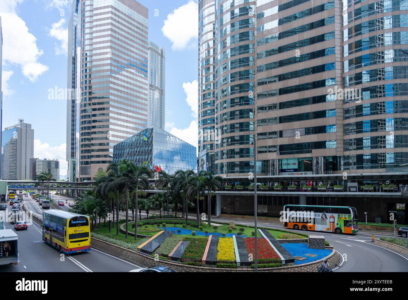 Hong Kong, Chine - 03 juillet 2024 : Une scène de rue à Hong Kong, Chine, avec de hauts gratte-ciel, des bus à impériale, des palmiers, et un rond-point avec f Banque D'Images