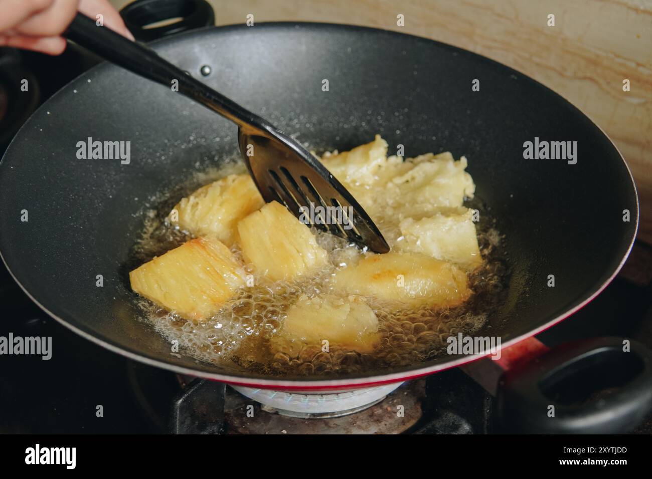 Une personne fait frire des tranches de manioc dans une poêle. Les tranches de manioc sont dorées et croustillantes. Banque D'Images