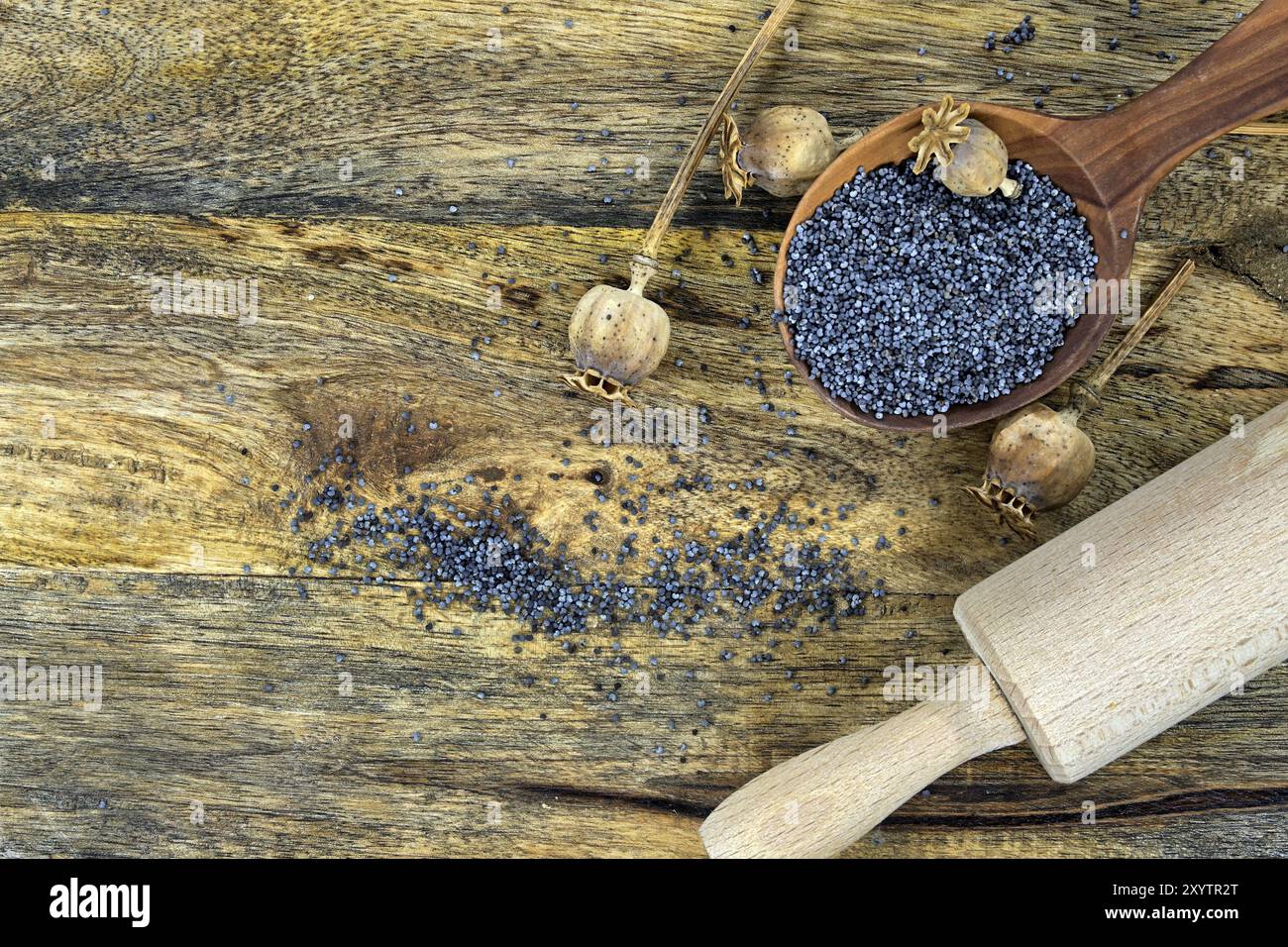 Cuillère en bois remplie de graines de pavot noir près d'un rouleau à pâtisserie placé sur une table rustique en bois altérée qui crée une scène chaleureuse et nostalgique Banque D'Images