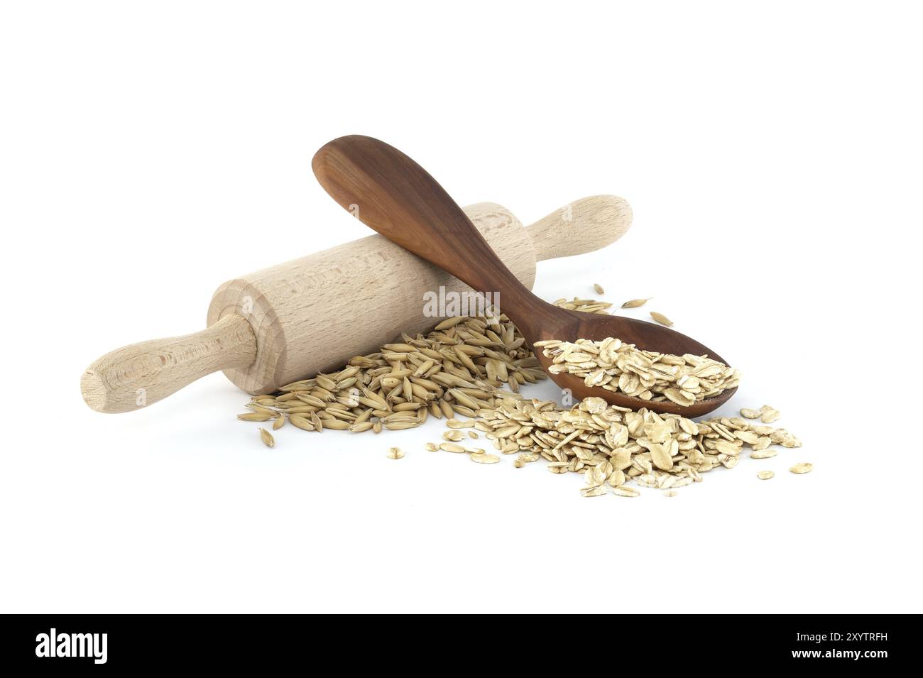 Grains d'avoine avec des coques ou des enveloppes près du rouleau à pâtisserie en bois et gruaux d'avoine roulés et aplatis en flocons dans une cuillère en bois isolée sur fond blanc Banque D'Images