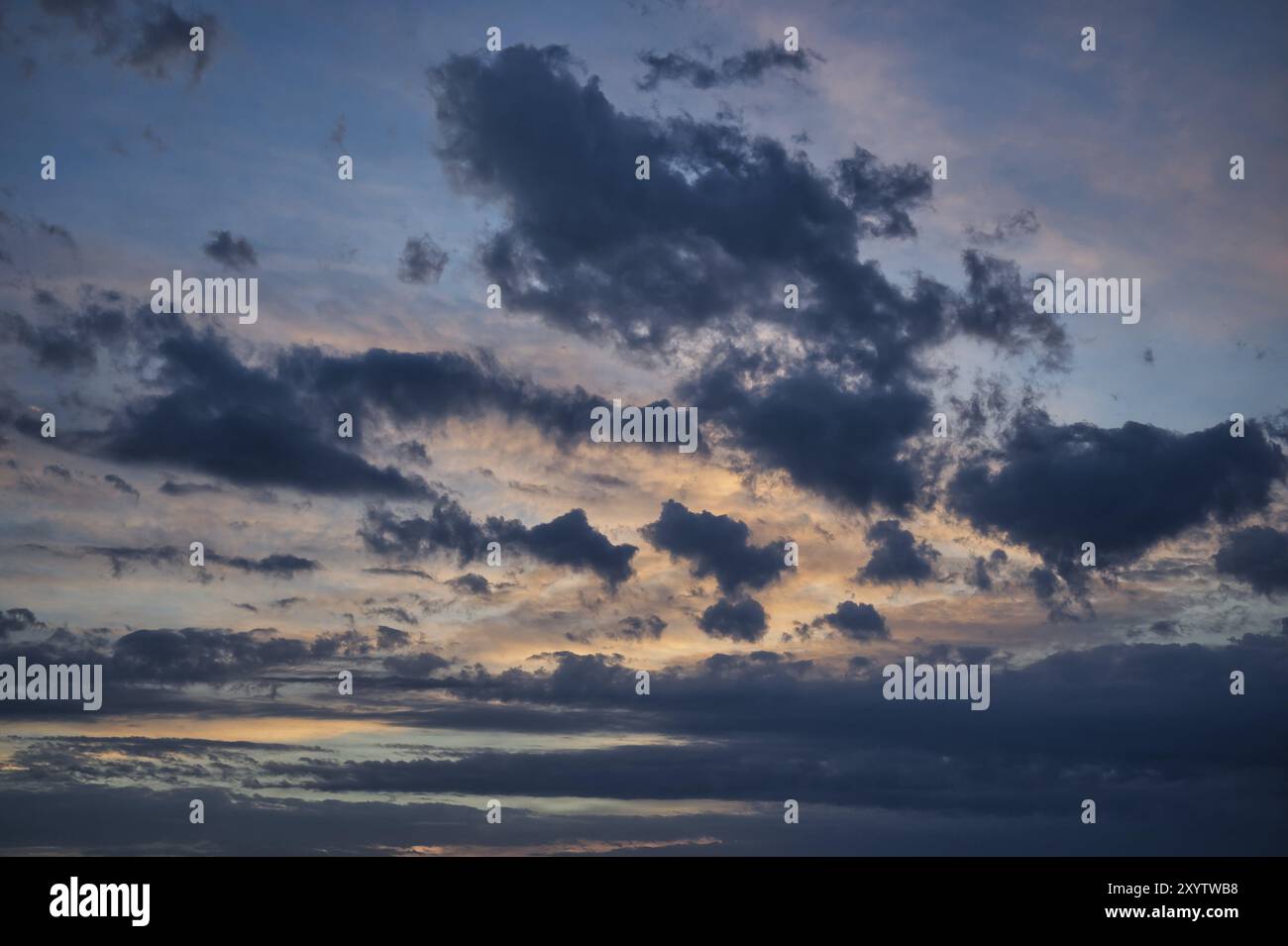Ciel orange et rose avec un soleil couchant derrière une couche de nuages blancs moelleux. Le soleil projette sur le h des rayons chauds teintés de couleurs du ciel du soir Banque D'Images