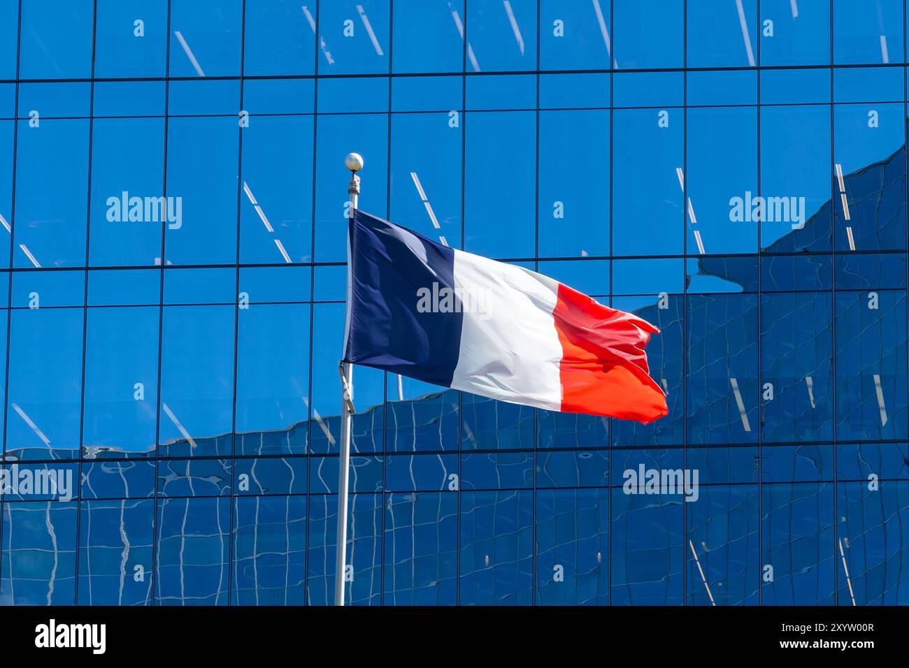 Un drapeau national de France agitant au vent avec un bâtiment en verre en arrière-plan. Banque D'Images