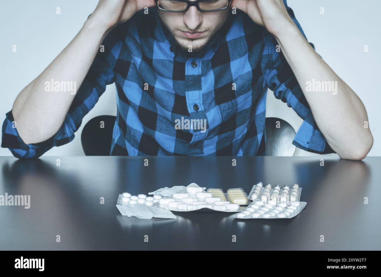 L'abus de drogues : Jeune homme assis sur une table, les médicaments et les pilules en face de lui Banque D'Images