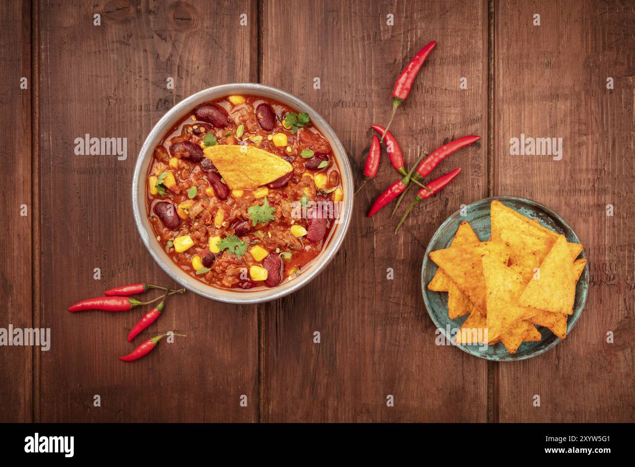 Chili con carne, un plat mexicain traditionnel avec des haricots rouges, des feuilles de coriandre, de la viande hachée et des piments, tiré au-dessus des nachos sur un rusti foncé Banque D'Images