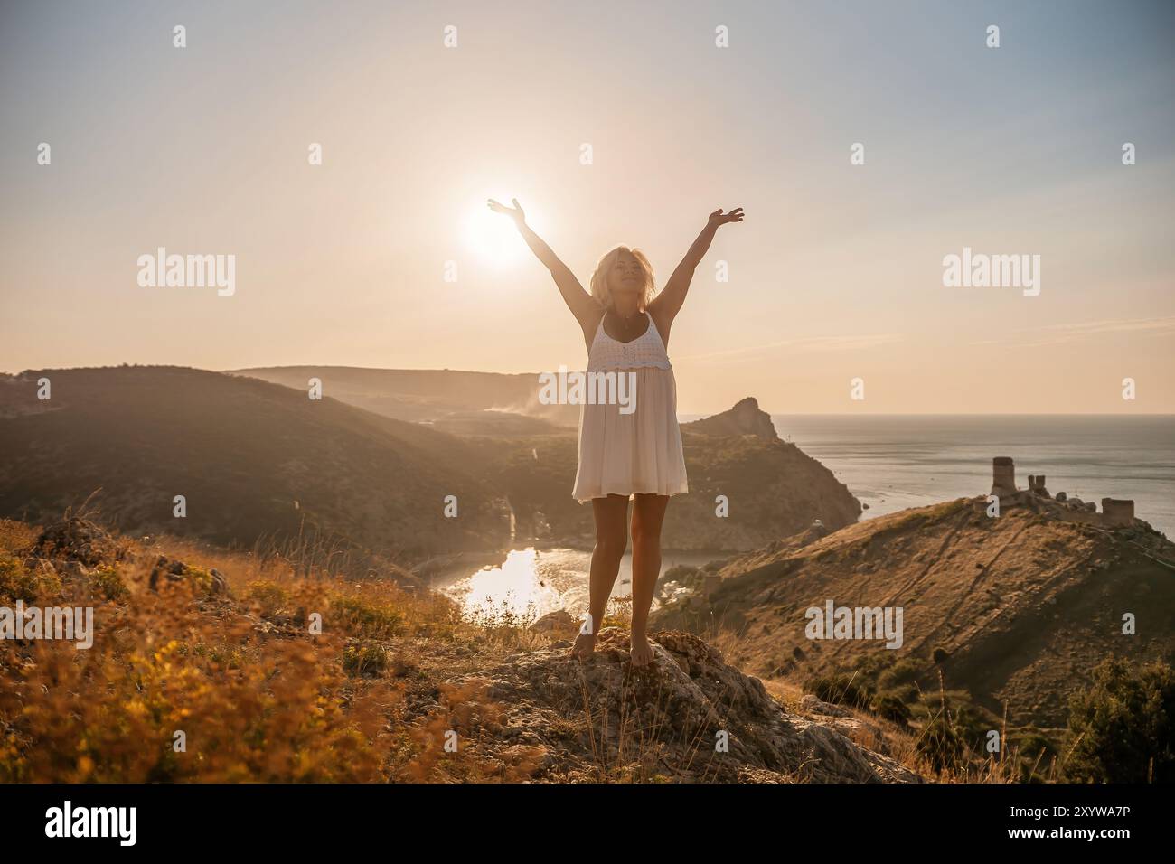 femme debout sur la colline avec les bras levés en l'air, regardant vers le soleil. La scène est paisible et sereine, avec l'expression de la femme véhiculant un Banque D'Images
