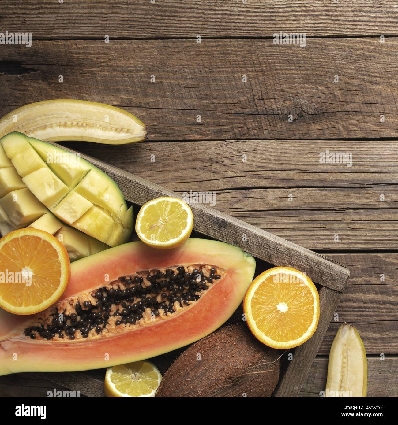 Fruits tropicaux frais dans une boîte de livraison en bois sur fond de bois. Papaye, orange, banane, noix de coco, mangue et citron vue de dessus plat avec copie sp Banque D'Images