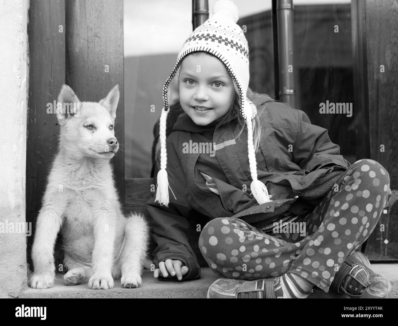 petite fille dans des vêtements d'hiver assis près du chien chiot husky sur une porte à l'extérieur Banque D'Images