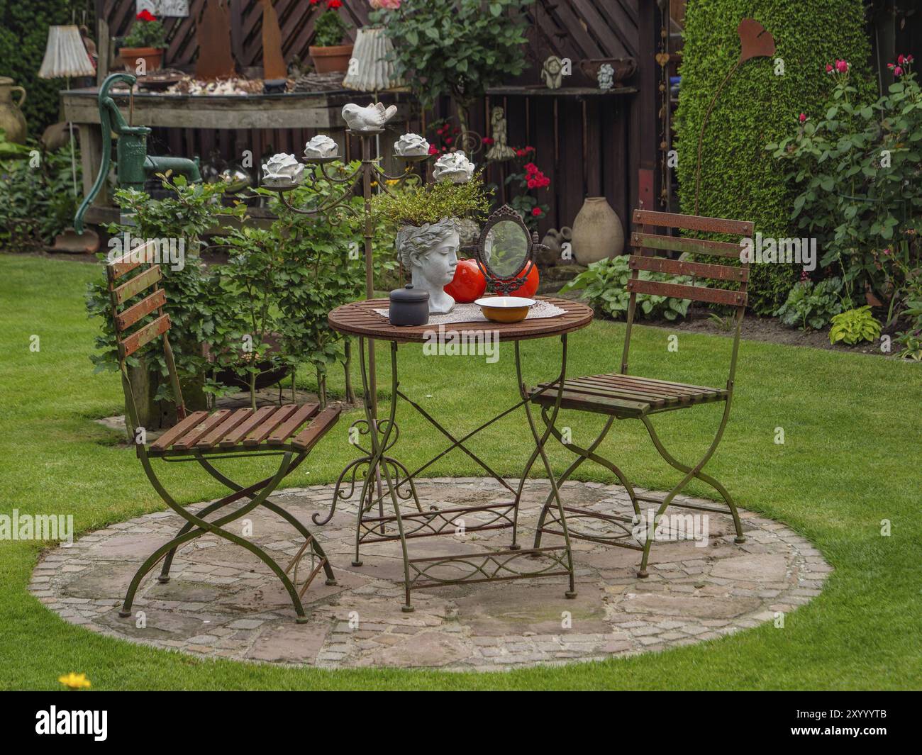 Table en métal et deux chaises sur une dalle de pierre dans le jardin, décorée d'un buste et de petites lampes, borken, muensterland, allemagne Banque D'Images