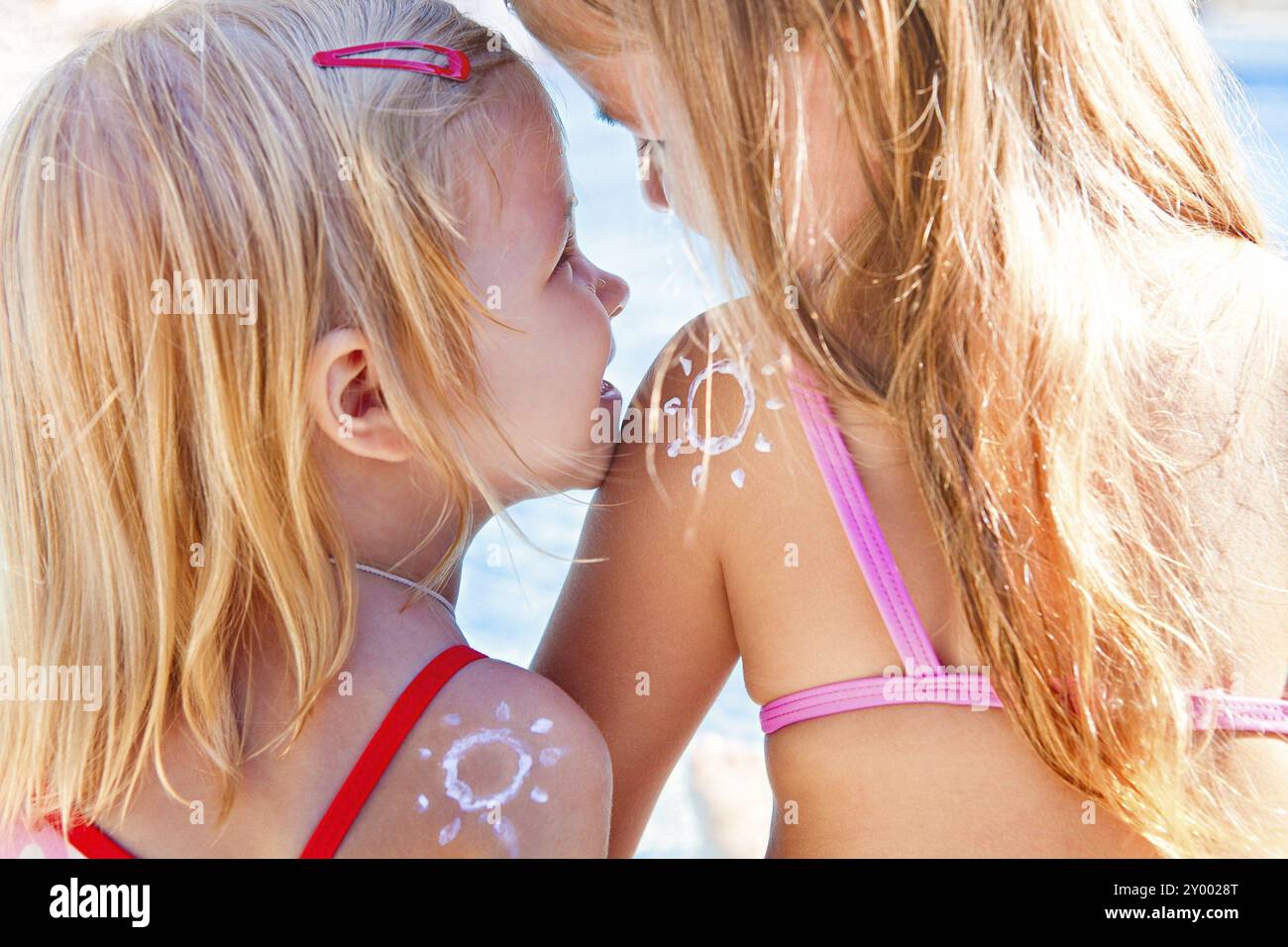 Portrait des sœurs de filles blondes heureuses avec de la crème sur les sholders en forme de rire de soleil et câlin au coucher du soleil. Vacances en famille et soleil protec Banque D'Images