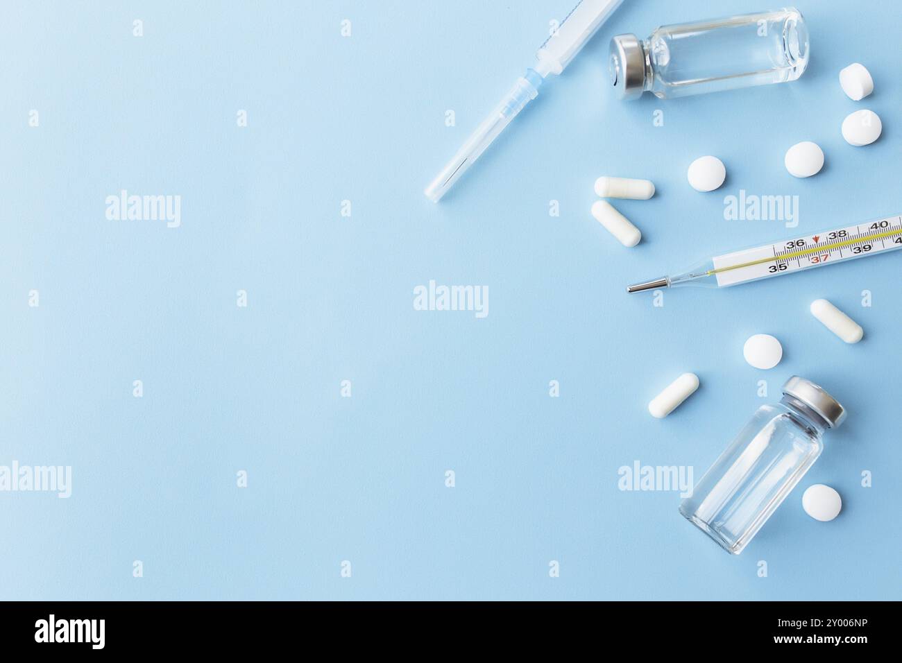 Traitement médicamenteux, concept vaccinal. Thermomètre, bouteilles de vaccin, injection, seringue, pilules sur fond bleu. Banque D'Images