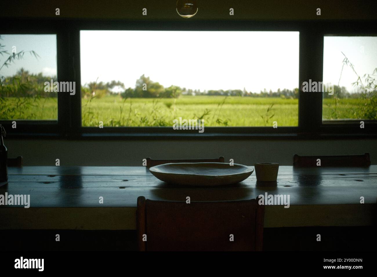 Coin repas îlot cuisine avec plateau en argile, tabouret de bar et fenêtre panoramique avec vue sur les rizières de la campagne Banque D'Images